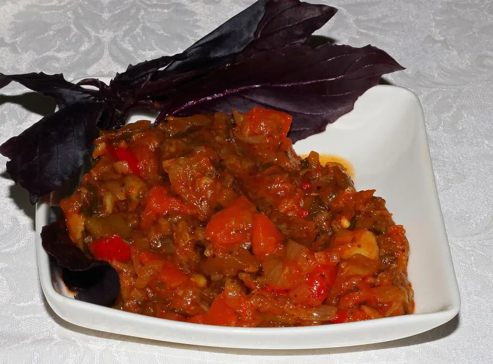 Ajapsandali stew in a white dish with purple basil