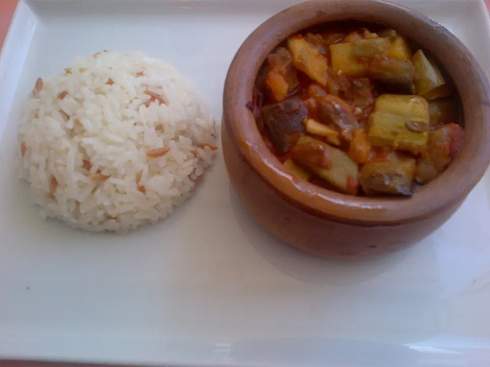 Türlü vegetable stew in a clay pot next to a mound of rice